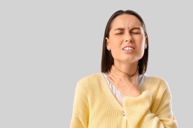 Gri arka planda boğaz ağrısı çeken genç bir kadın.