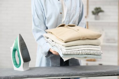 Elinde temiz giysiler ve ütüyle evde bekleyen genç bir kadın.