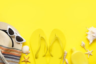 Şık terlikleri, plaj aksesuarları ve sarı arka planda deniz kabukları olan kompozisyon