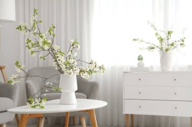 Oturma odasındaki koltuğun ve çekmecenin yanındaki sehpanın üzerinde çiçek açan bir vazo.