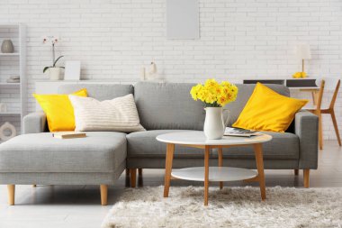 Şık oturma odasının içinde kanepe ve nergis çiçekli kahve masası var.