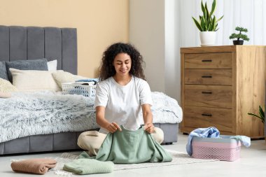 Güzel, genç, mutlu, Afro-Amerikan bir kadın, temiz giysileri katlıyor.