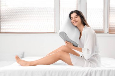 Pijamalı genç bir kadın yatakta yumuşak ortopedik yastık tutuyor.