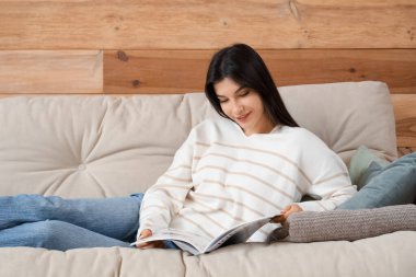 Genç bayan dergi okuyor ve oturma odasındaki rahat koltukta dinleniyor.