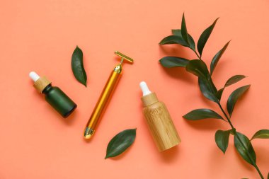Serumlu yüz masajı silindiri ve turuncu arka planda yeşil yapraklar.