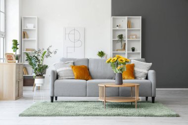 Oturma odasının içinde, kanepe, masa ve vazoda suni ayçiçekleri var.