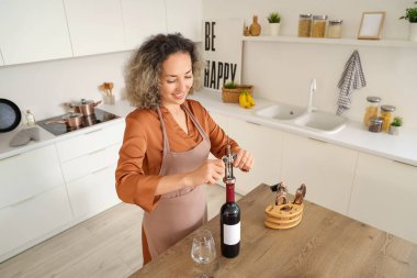 Güzel orta yaşlı kadın evde bir şişe şarap açıyor.