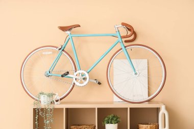 Odada bej duvarın yanında raf ve bisiklet var.