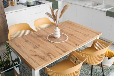 Yemek odasındaki ahşap masada otlu vazo.