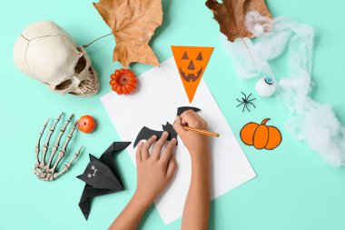 Malzemeleri olan çocuk turkuaz arka planda Cadılar Bayramı süslemeleri yapıyor