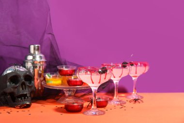 Mor arka planda turuncu masada Cadılar Bayramı dekoru olan kokteyller