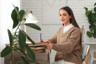 Kitaplarla dolu güzel, mutlu bir kız öğrenci masada ders çalışıyor.