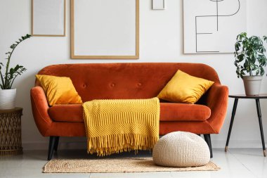 Kahverengi kanepe, ev çiçekleri ve resim çerçeveleri oturma odasındaki beyaz duvarda.