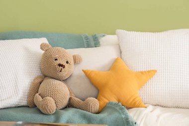 Yeşil duvarın yanındaki kanepede yastıklı ve ekoseli oyuncak ayı.