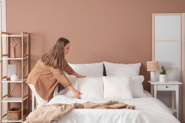 Modern yatak odasında yatak yapan güzel genç bir kadın.