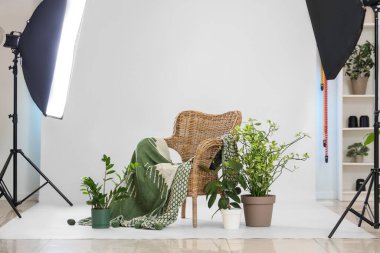 Çağdaş fotoğraf stüdyosunda çiçek ve ışıklandırma ekipmanları olan hasır bir koltuk.