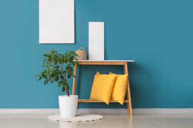Mavi duvarın yanında yastıklı konsol masası ve bitki örtüsü