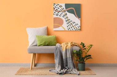 Yastıklı gri bir bank ve turuncu duvarın yanında rahat bir battaniye