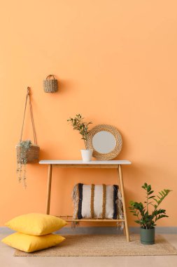 Yastıklı konsol masası ve turuncu duvarın yanındaki ev bitkisi
