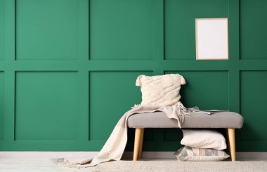 Yastıklı gri bank ve yeşil duvarın yanında battaniye