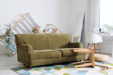 Yeşil kanepeli dağınık oturma odasının içi. Depremden sonra kahve masası ve raf üniteleri devrilmiş.