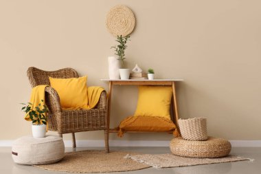 Yastıklı konsol masası, ev bitkileri ve bej duvarın yanındaki hasır koltuk.