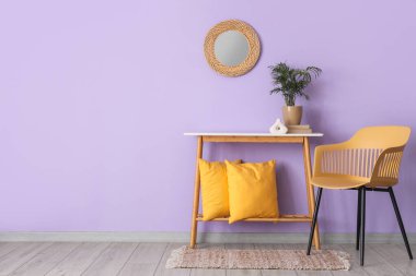 Yastıklı konsol masası, leylak duvarın yanındaki ev bitkisi ve sandalye.