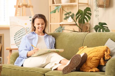 Genç bayan ressam kanepede oturup resim çiziyor.