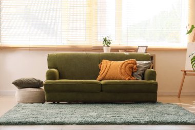 Şık oturma odasının penceresinin yanındaki yumuşak yastıklı rahat yeşil kanepe.