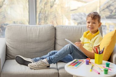 Küçük çocuk kanepede oturuyor ve oturma odasında çizim yapıyor.