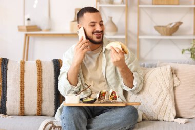 Lezzetli Meksika tacoları olan genç adam mutfakta cep telefonuyla konuşuyor.