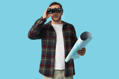 Haritası olan genç bir turist mavi arka plandaki dürbünlerden bakıyor. Güzergah kavramı