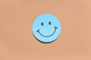 Kahverengi arka planda gülen yüzlü yapışkan bir not.