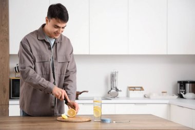 Evde eritilmiş su için limon kesen yakışıklı genç adam.