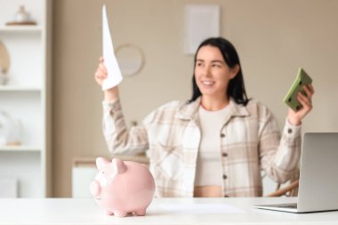 Evinde hesap makinesi ve para iadesi olan mutlu bir kadına karşı kumbarayı masaya yatırın.