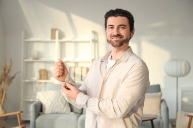 Yakışıklı genç adam, evde şık beyaz gömleğini ilikliyor.