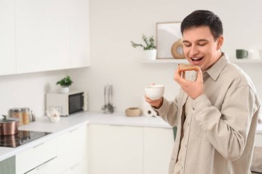 Genç adam mutfakta fıstık ezmeli tost ve çay tutuyor.