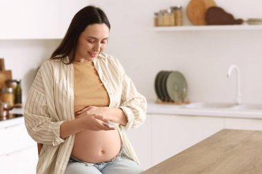 Genç hamile kadın mutfakta glukometre kullanıyor. Gebelik Diyabet Konsepti