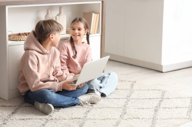 Genç bir çocuk kız kardeşiyle mutfakta dizüstü bilgisayar kullanıyor.