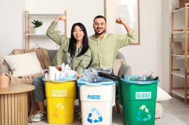 Çöpleri çöp bidonlarına dizip evde kaslarını gösteren genç bir çift. Küresel Geri Dönüşüm Günü