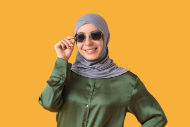 Sarı arka planda tesettürlü ve şık güneş gözlüklü güzel Müslüman kadın.