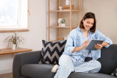 Evdeki koltukta modern tablet bilgisayar kullanan genç bir kadın.