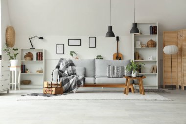 Gri kanepesi, çiçekleri ve raf üniteleri olan şık bir oturma odası.