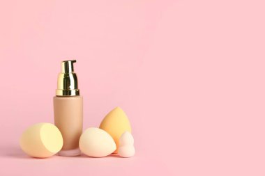 Pembe arka planda makyaj süngeri ve bir şişe fondöten.