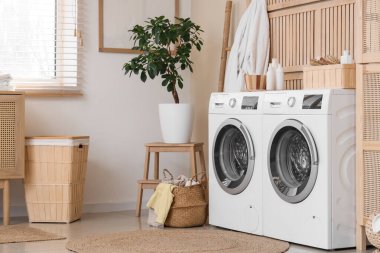 Modern çamaşır makineleri, hasır sepeti ve banyo aksesuarları olan şık bir çamaşırhane.