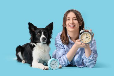 Güzel genç bir kadın ve mavi arka planda alarm saatleri ve uyku maskesi olan sevimli bir Sınır Köpeği Collie.