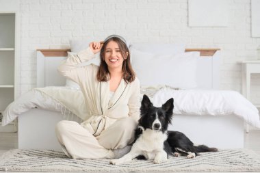 Uyku maskesiyle güzel bir genç kadın ve evde yatağın yanında oturan sevimli bir Border Collie köpeği.