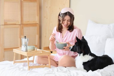 Uyku maskesiyle, kahvaltısıyla ve Collie 'nin tatlı köpeğiyle evde oturan güzel genç bir kadın.