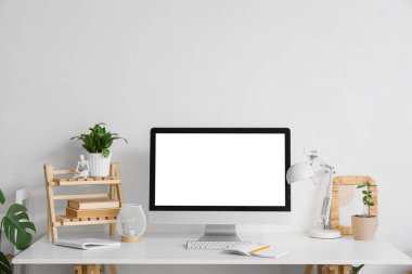 Beyaz duvarın yanında modern bilgisayar, lamba ve ev bitkileriyle rahat çalışma alanı