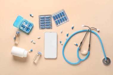 Bej arka planda cep telefonu, ilaçlar ve steteskop.